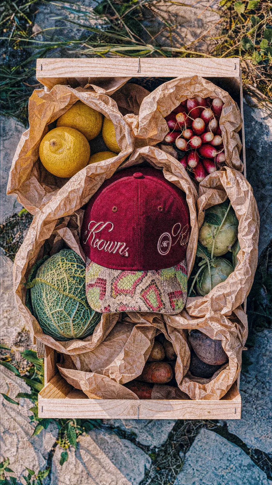 Casquette bordeaux posée parmi des fruits, du papier et une caisse en bois.