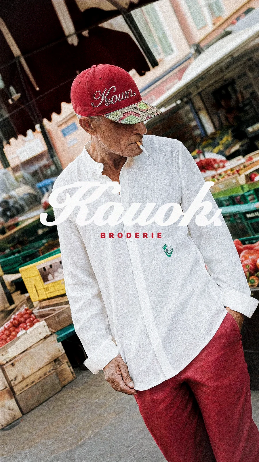 Personne en chemise blanche et casquette bordeaux, avec le lettrage Kouoh Broderie.